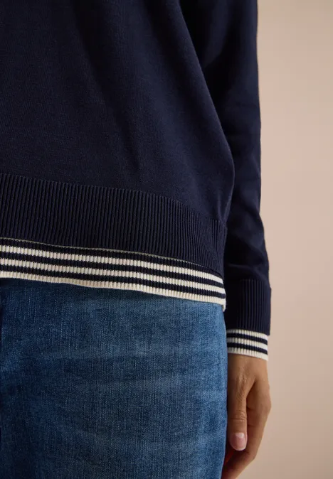 Pull à col rond avec détail superposé urban dark blue Pull bleu marine à rayures blanches aux manches et à l’ourlet, porté sur un pantalon en jean bleu.