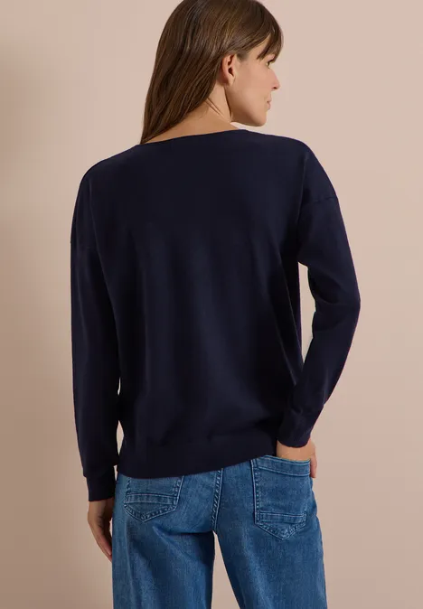 Pull à manches longues et col en V arrondi urban dark blue Femme de dos portant un pull bleu marine et un jean sur fond neutre.