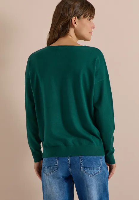 Eine Frau mit dunkelgrünem Pullover und Jeans, vom Rücken in Profilansicht.