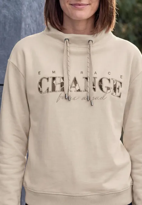 Sweat-shirt avec inscription et col cheminée pearl beige Eine Person trägt einen beigen Kapuzenpullover mit dem Schriftzug ‚Embrace CHANGE live loud‘, frontal abgebildet.
