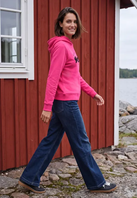 Sweatshirt mit Details in Rippstruktur pink flash Frau in pinkem Hoodie und Schlagjeans lächelnd vor rotem Holzhaus am Wasser.