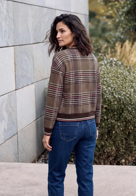 Eine Frau in karierter Jacke und Jeans lehnt an einer Steinmauer und blickt zurück.