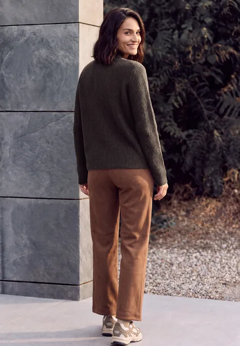 Trui met col en vlechtpatroon truffle brown melange Eine lächelnde Frau steht in grüner Strickjacke und braunen Hosen, blickt über die Schulter im Außenbereich.