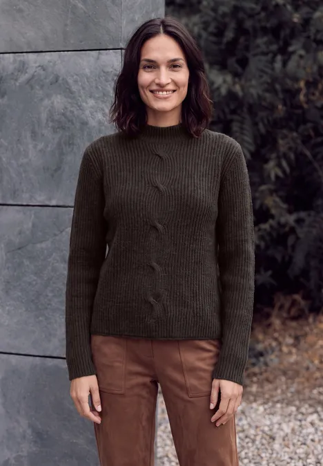 Trui met col en vlechtpatroon truffle brown melange Eine Frau mit dunklem Strickpullover und braunen Hosen steht im Freien und lächelt.