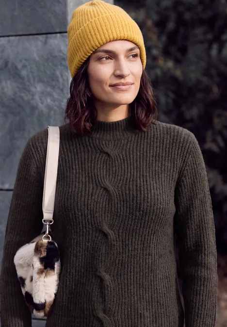 Trui met col en vlechtpatroon truffle brown melange Frau mit gelber Strickmütze und dunkelgrünem Pullover, trägt eine kleine Felltasche.