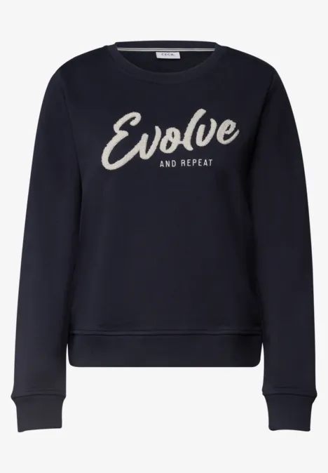 Dunkler Sweatpullover mit dem weißen Schriftzug ‘Evolve and Repeat’ auf der Vorderseite.