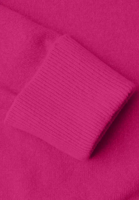Close-up van een felroze gebreide trui met omgeslagen mouwboord.