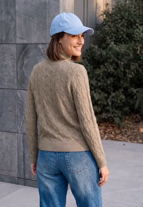 Eine junge Frau in Jeans, braunem Pullover und blauer Cap blickt lächelnd über die Schulter.