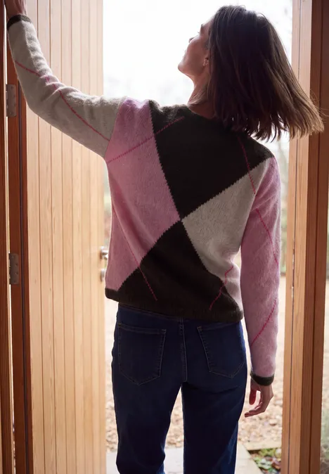 Pullover mit Rundhals und Argyle-Muster truffle brown Eine Frau mit Rautenmuster-Pullover in Pink, Grau und Dunkelgrün öffnet von hinten eine Holztür.