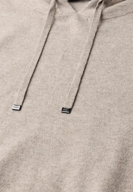 Beige Kapuzenpullover mit Kordelzug im Detail, weiche Struktur sichtbar.