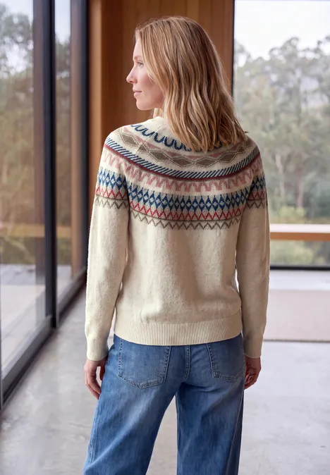 Pullover mit Rundhals und Jacquardmuster oat milk beige melange Frau mit hellem Fair-Isle-Pullover und Jeans steht in hellem Raum vor großen Fenstern