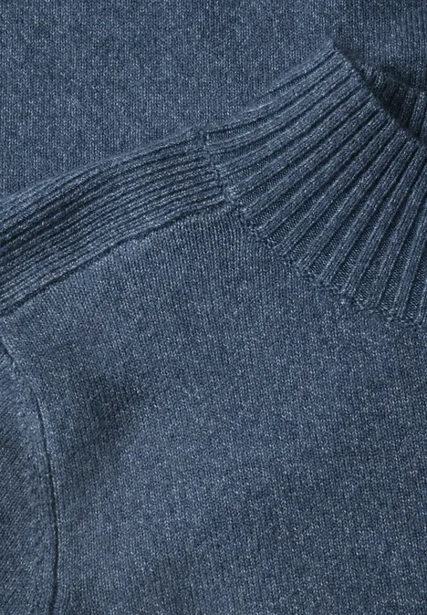 Gros plan d'un pull en maille bleu foncé à col roulé et texture raffinée.