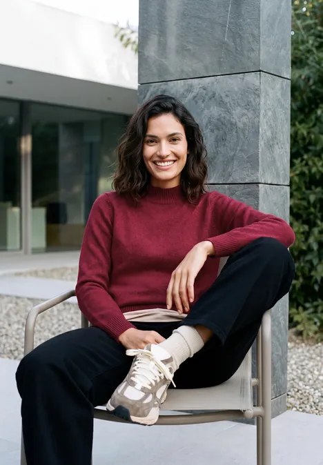 Une femme souriante est assise confortablement sur une chaise devant un bâtiment moderne.