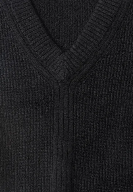 Nahaufnahme eines schwarzen, V-förmigen Strickpullovers mit sichtbarer Struktur.