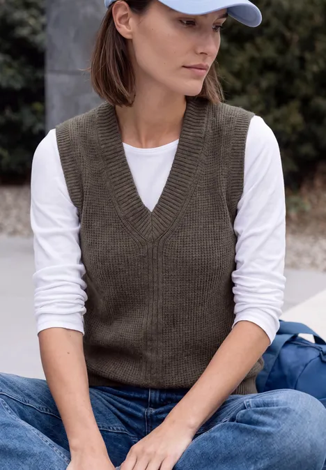 Pullunder in Unifarbe mit V-Neck mushroom taupe melange Eine Frau sitzt draußen mit weißem Langarmshirt, brauner Strickweste, Jeans und weißer Baseballkappe.