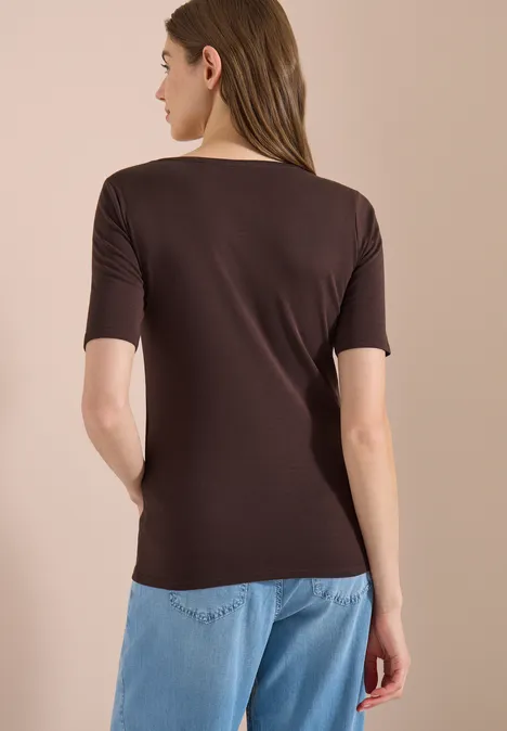 Vrouw van achteren in een bruin kort mouwshirt en lichtblauwe jeans voor een neutrale achtergrond.