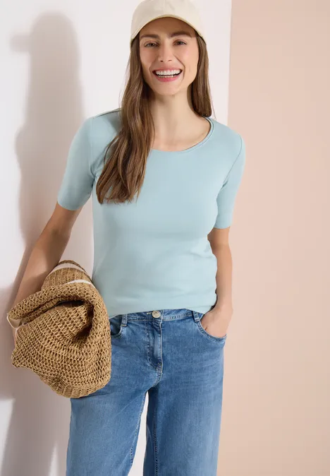 Vrouw in lichtblauw T-shirt en spijkerbroek met een strozak voor een lichte achtergrond.