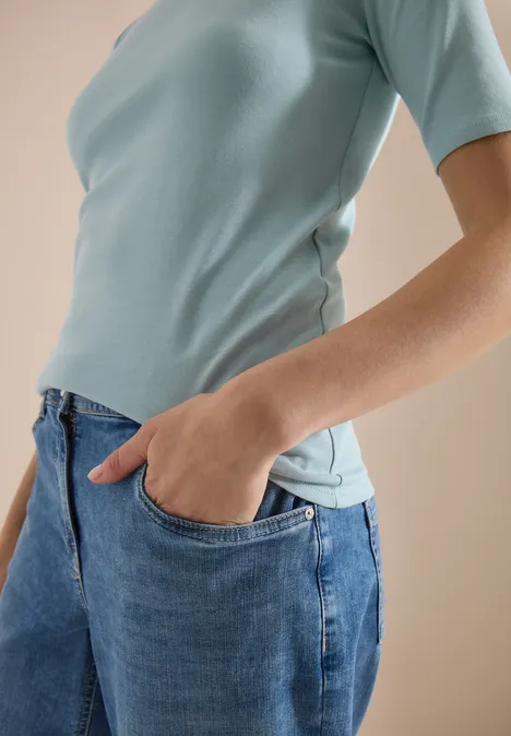 Bovenlichaam van iemand in lichtblauw T-shirt, hand in de zak van een blauwe jeans.