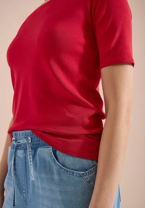 Bovenlichaam van een persoon in een rood T-shirt met korte mouwen en een blauwe jeans