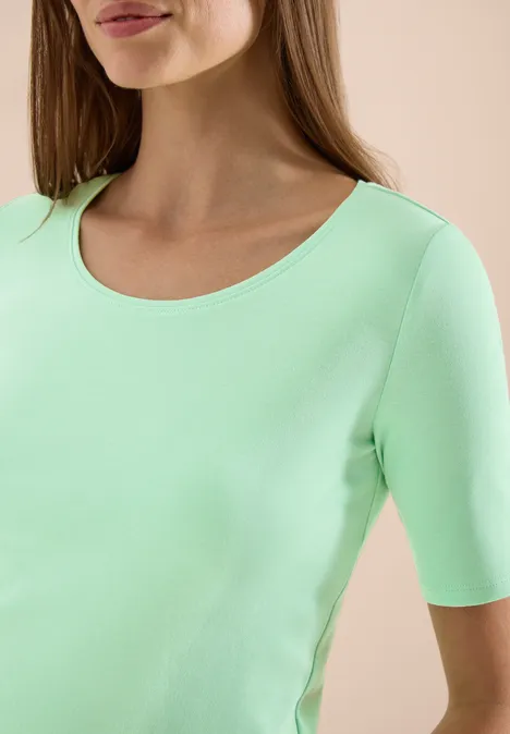 Oberkörper einer Frau in mintgrünem, kurzärmeligem Shirt mit rundem Ausschnitt.