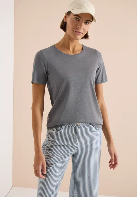 Basic Shirt met ronde hals graphite light grey Een persoon draagt een eenvoudig grijs T-shirt en een blauw-wit gestreepte broek.