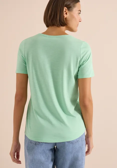 Person von hinten in mintgrünem T-Shirt und blauen Jeans vor hellem Hintergrund