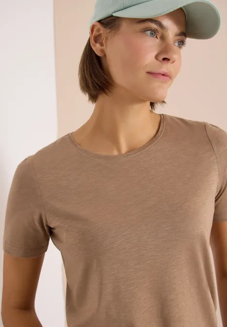 Basic T-Shirt mit Rundhals in Unifarbe creamy mocha Frau trägt beige T-Shirt und hellgrüne Baseballkappe vor neutralem Hintergrund.