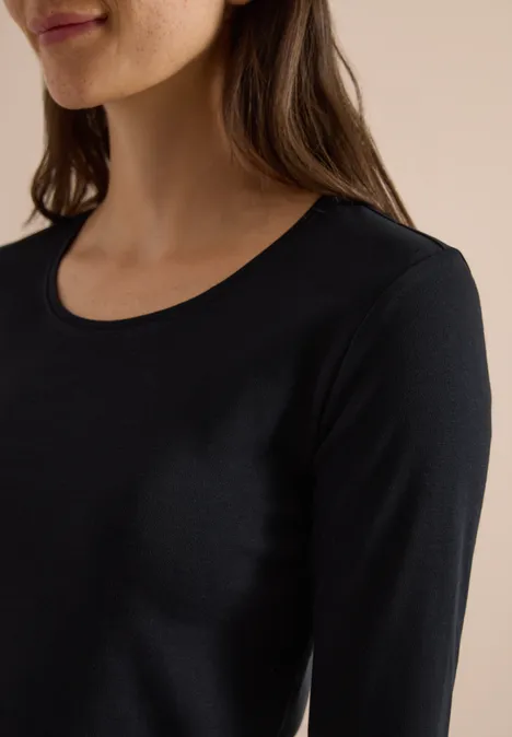 Eine Frau trägt ein schlichtes schwarzes Langarmshirt mit rundem Ausschnitt.
