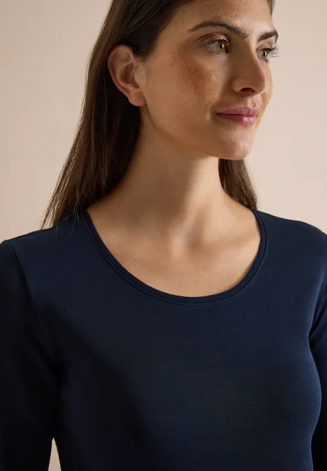 Eine junge Frau mit braunen Haaren trägt ein dunkelblaues Langarmshirt und blickt seitlich.