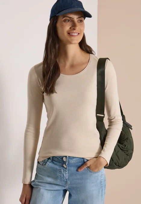 Basic Langarm Shirt mit Rundhals pearl beige Frau lächelt, trägt beiges Langarmshirt, Jeans, blaue Kappe und grüne Tasche über der Schulter.