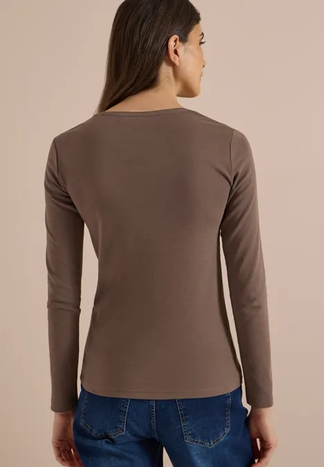 Frau von hinten in braunem Langarmshirt und blauen Jeans vor hellem Hintergrund.