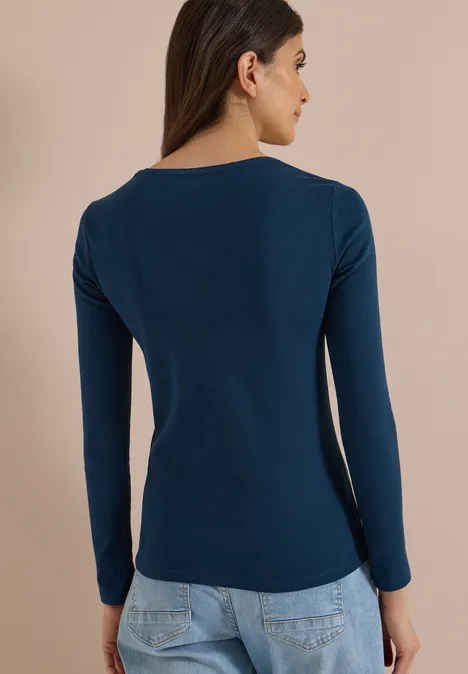 Frau von hinten in Navy-Blau Langarmshirt und Jeans vor neutralem Hintergrund.