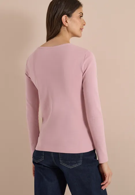 Frau von hinten in rosafarbenem Langarmshirt und blauen Jeans vor hellem Hintergrund