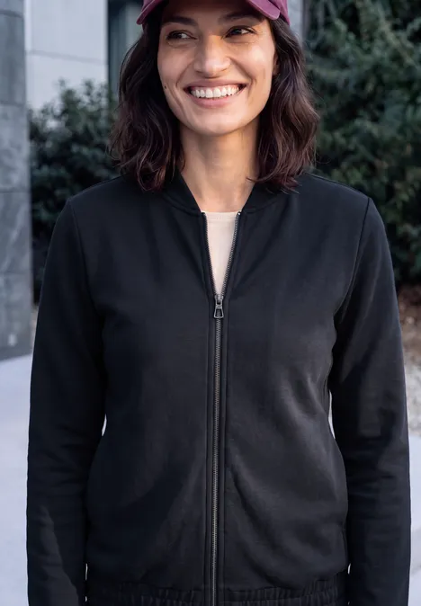 Eine gut gelaunte Frau im Freien trägt schwarze Jacke, weißes Shirt und rote Baseball-Kappe.