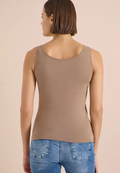 Frau von hinten in braunem Tanktop und Jeans vor neutralem Hintergrund.