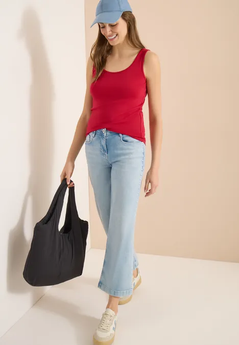 Femme en débardeur rouge, jean bleu clair, baskets et casquette, sac noir oversize.