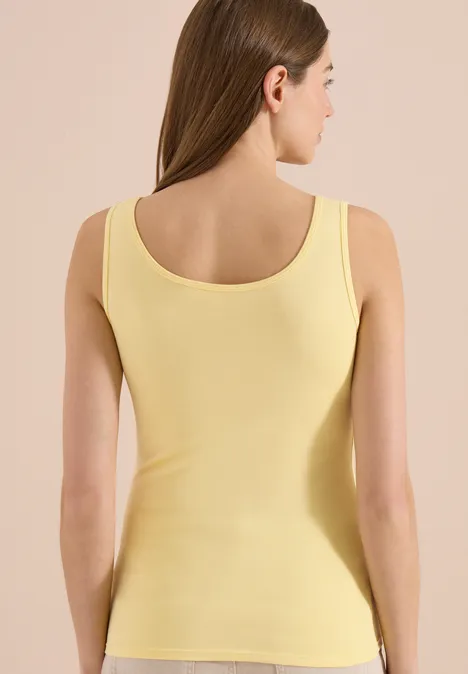 Eine Frau in einem gelben ärmellosen Top, von hinten aufgenommen.