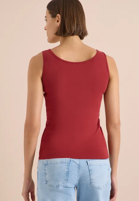 Femme de dos, débardeur rouge et jean bleu, fond neutre.