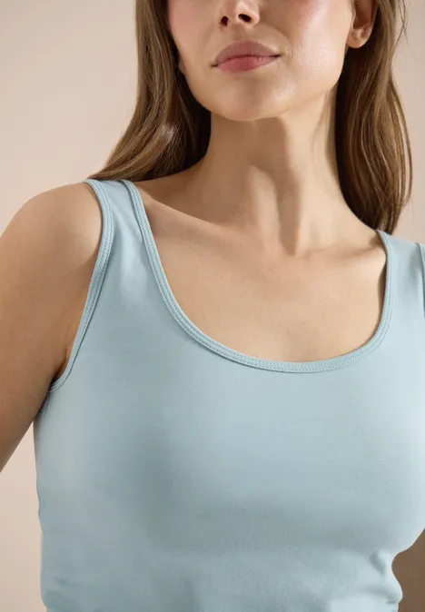 Vrouw in een lichtblauw hemdje, close-up van schouders en torso.