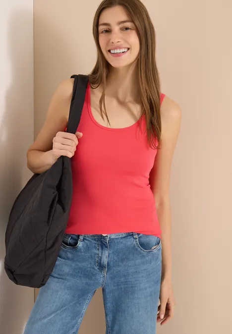 Femme en débardeur rouge, jean et sac noir sur fond clair.