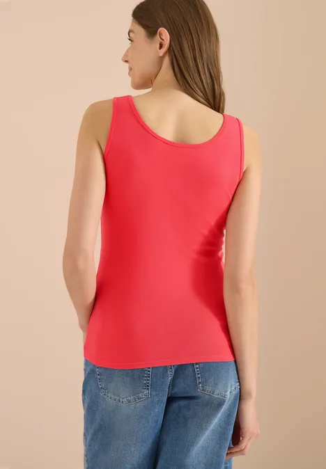Femme de dos portant un débardeur rouge et un jean bleu sur fond clair.