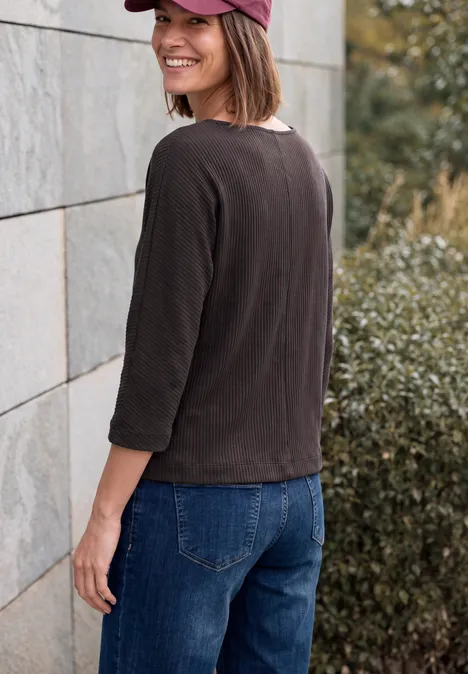 Shirt im Two-Tone-Look mit Boat Neck truffle brown Frau blickt lächelnd über die Schulter, trägt dunkles Oberteil, Jeans und Cap, steht an einer Steinwand
