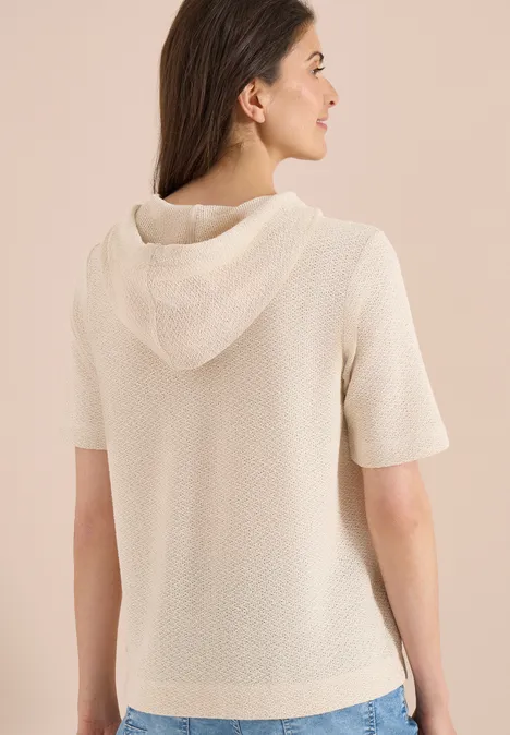 Vrouw van achteren in een korte, gebreide crèmewitte hoodie tegen een neutrale achtergrond.