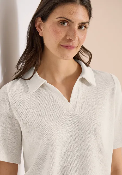 Vrouw met wit, kort mouw polo met open V-hals voor een neutrale beige achtergrond.