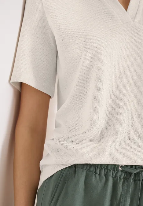 Iemand draagt een lichtbeige T-shirt met korte mouwen en V-hals en een donkergroene losse broek met koord.