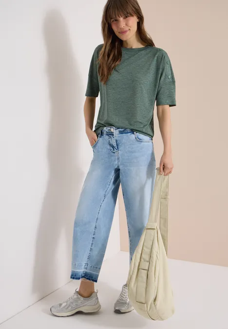 Persoon draagt groen T-shirt, lichte jeans, grijze sneakers en een beige tas.