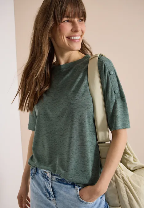 Vrouw in groen T-shirt met korte mouwen en knopen, blauwe jeans en rugzak over de schouder