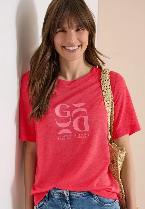 Frau trägt rotes T-Shirt mit Aufdruck und Korbtasche über der Schulter