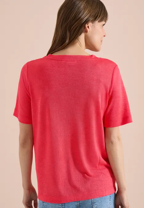 Rückansicht einer Frau mit rotem T-Shirt vor neutralem Hintergrund.