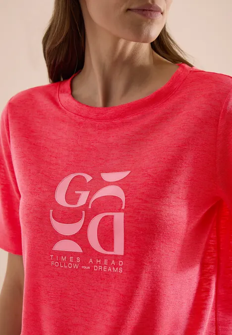 Nahaufnahme einer Frau im pinkroten T-Shirt mit Schriftzug 'GOA' und Slogan 'times ahead follow our dreams'.